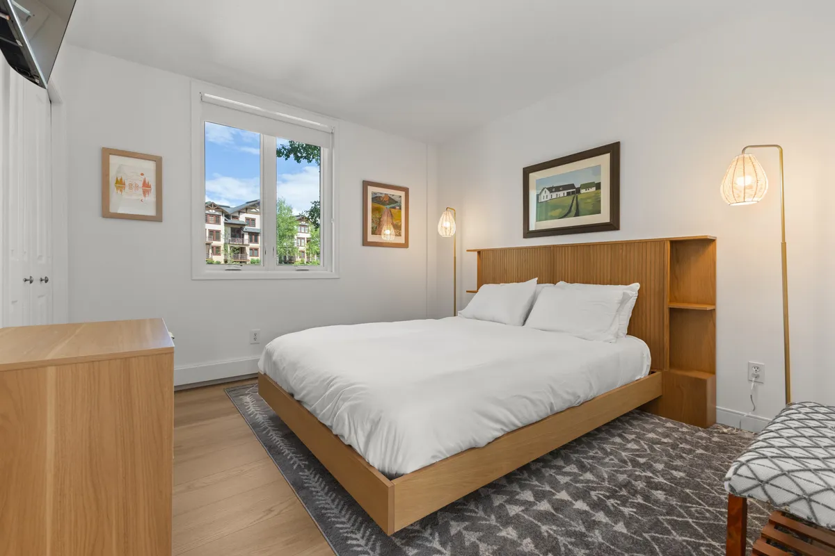 A tranquil bedroom filled with soft, natural light from the window, a comfortable bed with crisp bedding, decorative artwork, and gentle lighting fixtures that create a peaceful ambiance. The setting is ideal for restful nights and quiet mornings.