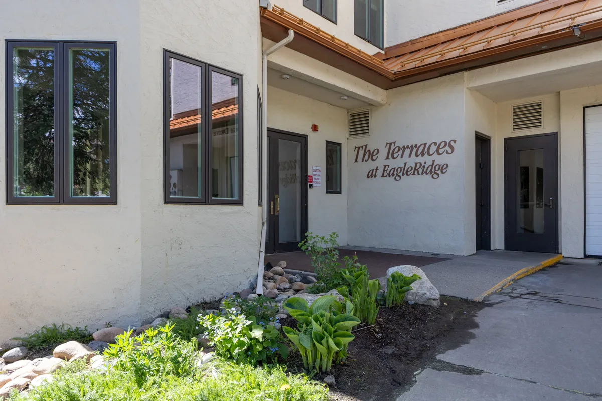 A welcoming view of the building's entrance, surrounded by a landscaped garden and clear signage, suggesting a friendly, communal atmosphere. The scene captures the start of a family's adventure as they depart or arrive for summer activities and events.