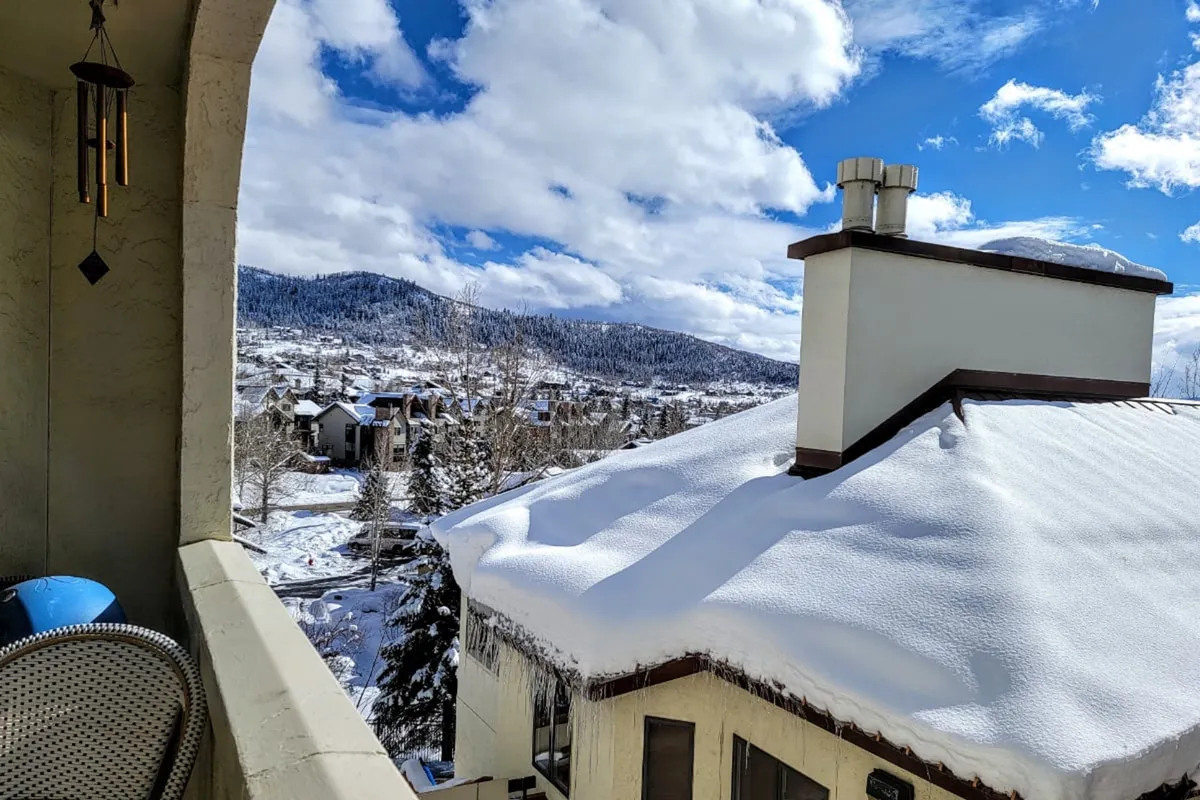 A stunning winter view of snow-covered rooftops with the mountains rising beyond, set under a cloudy sky. The vantage point suggests a sense of immersion in the alpine environment, capturing the allure of Steamboat during ski season.