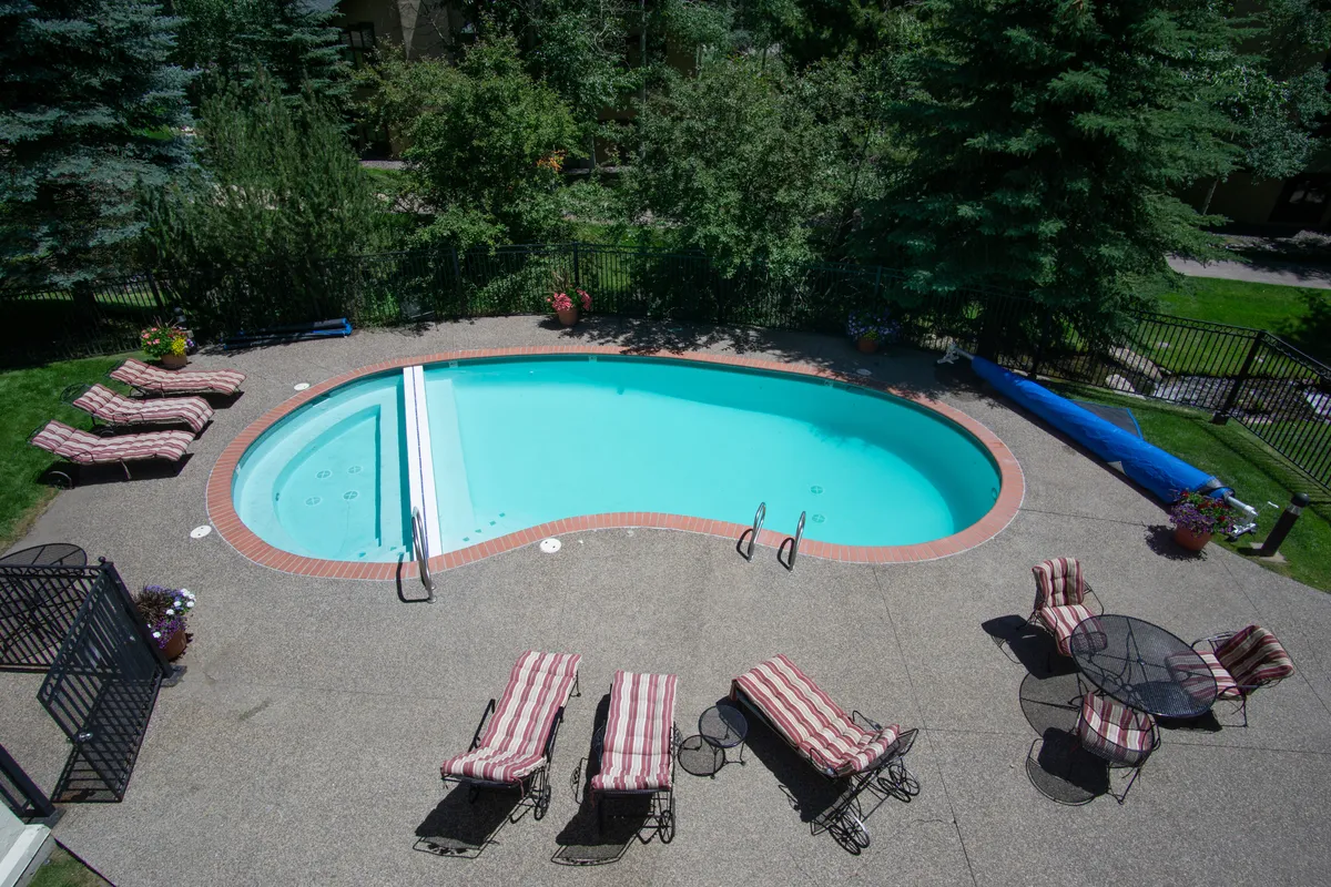 A vibrant exterior view of the swimming pool, with lounge chairs, a patio table, and lush greenery. The inviting setup alludes to resort-style amenities and leisure opportunities just steps from your door.