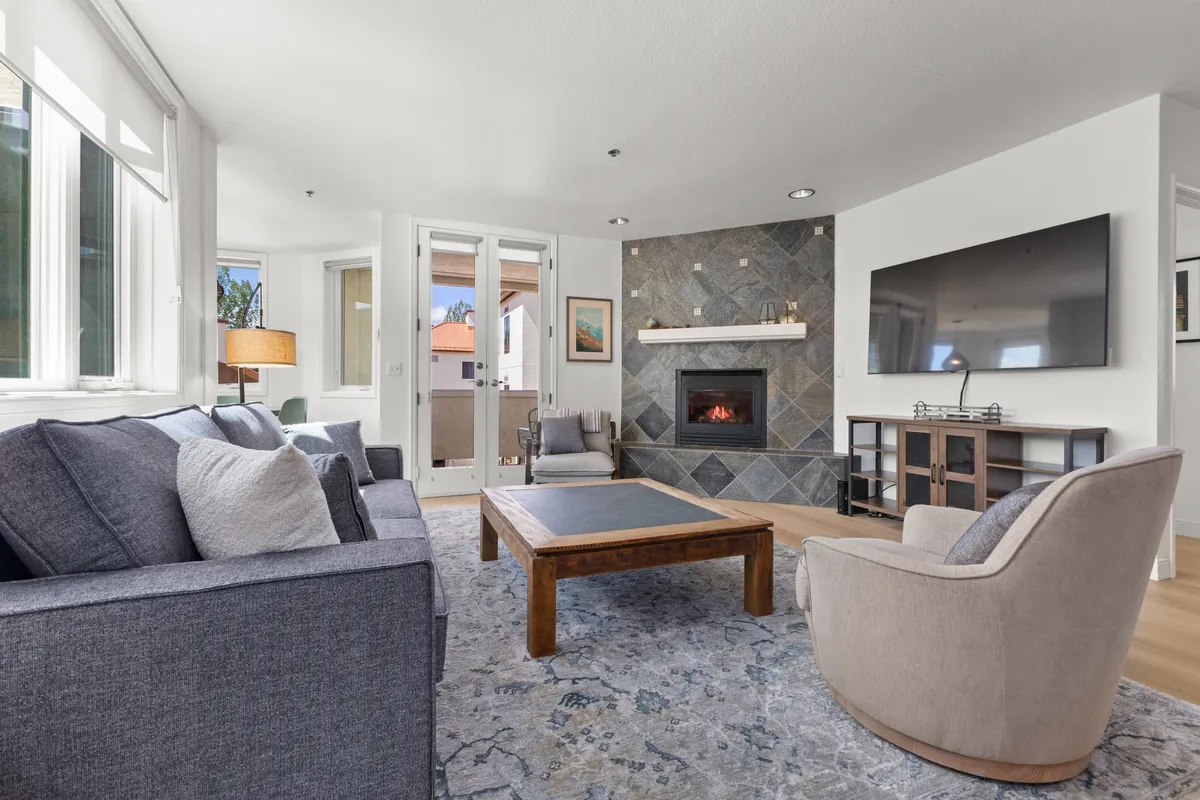 The image showcases a warmly decorated living room featuring a glowing fireplace, a comfortable sofa, a stylish coffee table, and a mounted television. Sunlight streams into the room, creating a bright and inviting atmosphere that encourages relaxation and socializing.