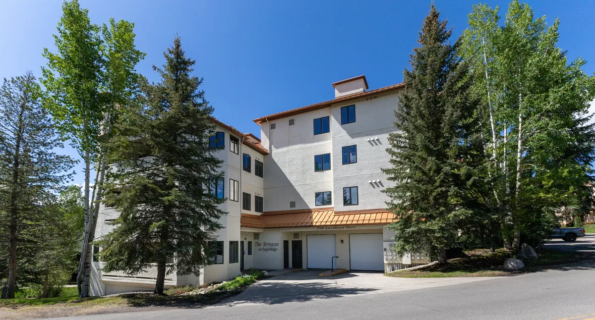 This image features the building facade surrounded by trees and a welcoming entrance area. The setting is calm and inviting, with visible pathways that suggest easy access to local amenities and a relaxing environment for extended stays.