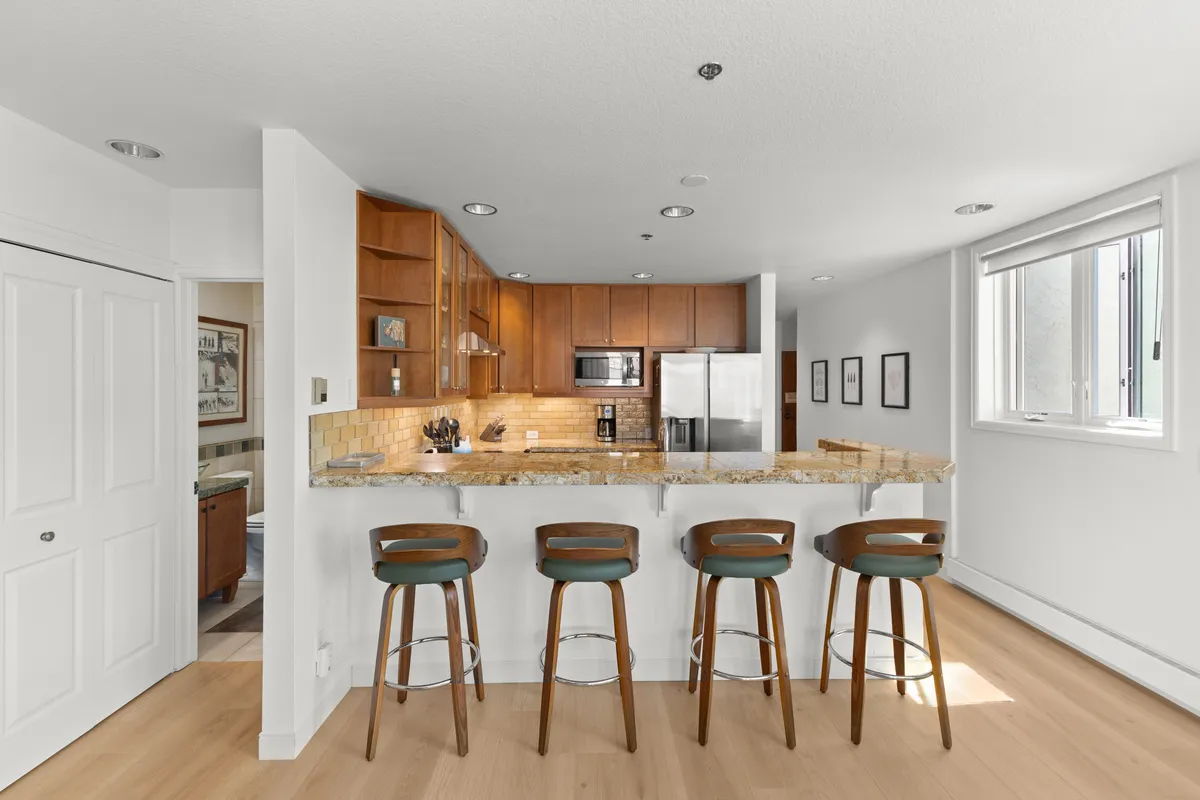 A modern kitchen with granite countertops, wood cabinetry, and stainless steel appliances. Bar stools line the kitchen island, creating a spot for casual dining or socializing while meals are being prepared.