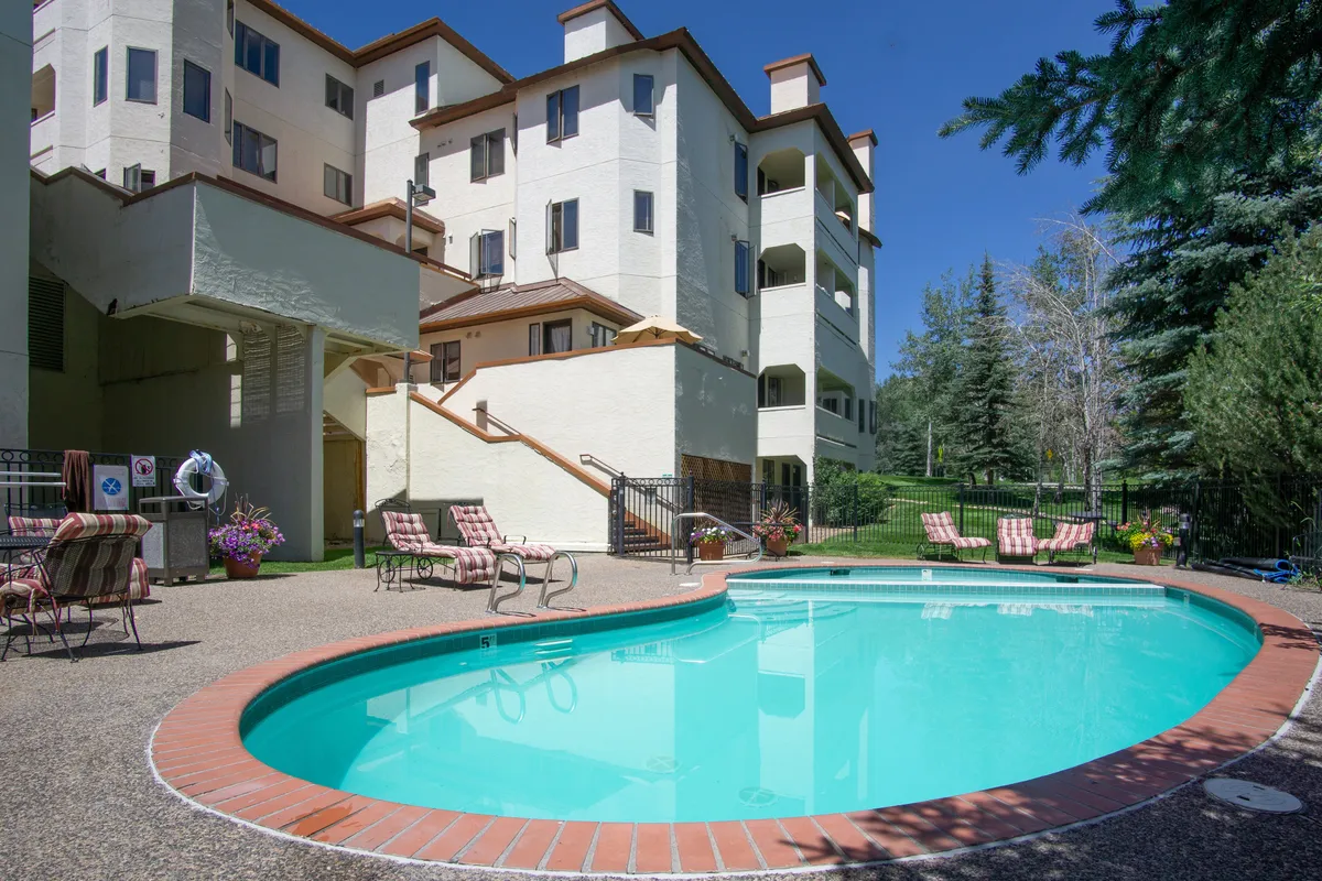 This exterior image shows a sparkling swimming pool with inviting lounge chairs set around it, adjacent to the building's facade. The landscaped area surrounding the pool is lush and green, creating a tranquil and resort-like environment.