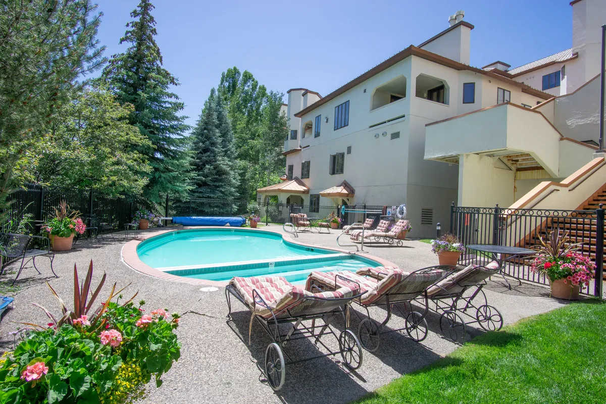 Featuring a swimming pool bordered by lounge chairs and surrounded by lush greenery, this image exudes relaxation and leisure. The setting suggests both social gatherings around the pool and quiet moments enjoying the outdoors, whether in the sun or shade.