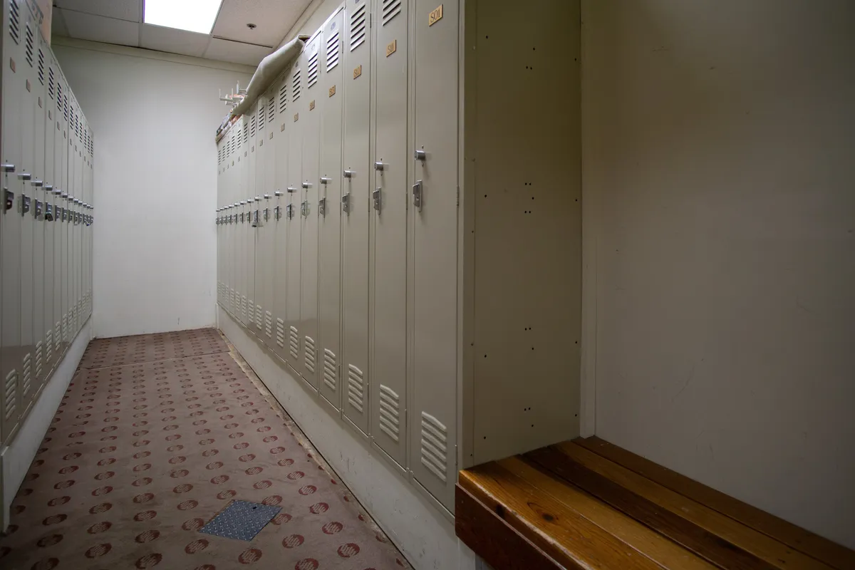 A practical interior space featuring metal lockers, a wooden bench for seating, and a neutral carpeted floor. The setting is clearly designed for changing clothes and storing personal items.
